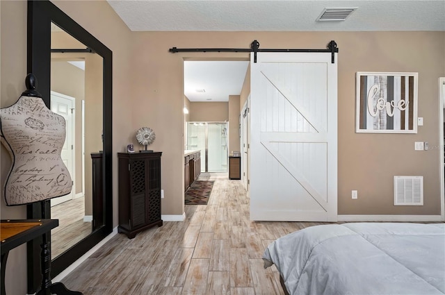 bedroom with a barn door, a textured ceiling, light hardwood / wood-style floors, and ensuite bath