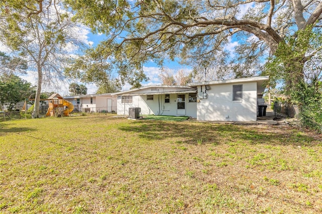 back of house with central AC, a lawn, and a playground