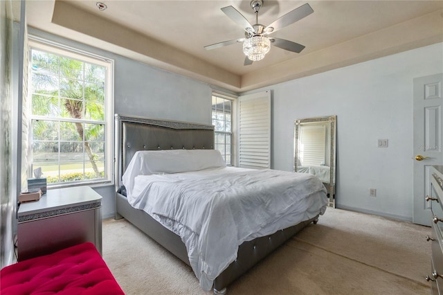 bedroom featuring multiple windows, a raised ceiling, light colored carpet, and ceiling fan