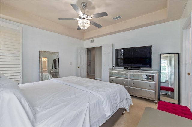 bedroom with a tray ceiling, light colored carpet, and ceiling fan