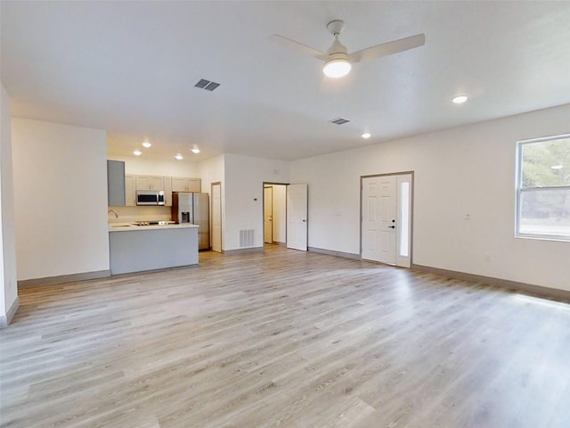 unfurnished living room featuring visible vents, baseboards, and a ceiling fan
