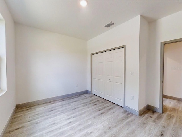 unfurnished bedroom with a closet, light wood finished floors, baseboards, and visible vents