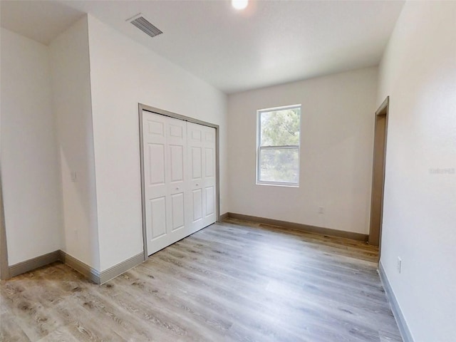 unfurnished bedroom featuring visible vents, baseboards, light wood finished floors, and a closet