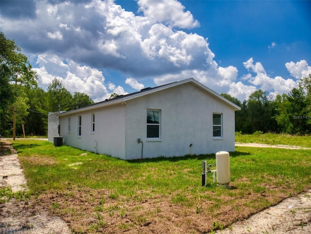 view of home's exterior with stucco siding, central AC, and a lawn