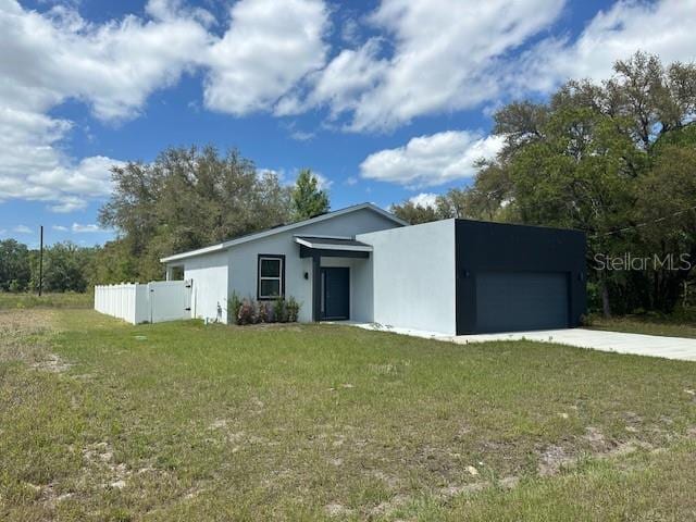 view of front of home with a front yard, an attached garage, concrete driveway, fence, and stucco siding