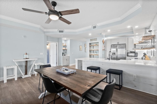 dining room with sink, dark hardwood / wood-style flooring, a tray ceiling, crown molding, and a textured ceiling