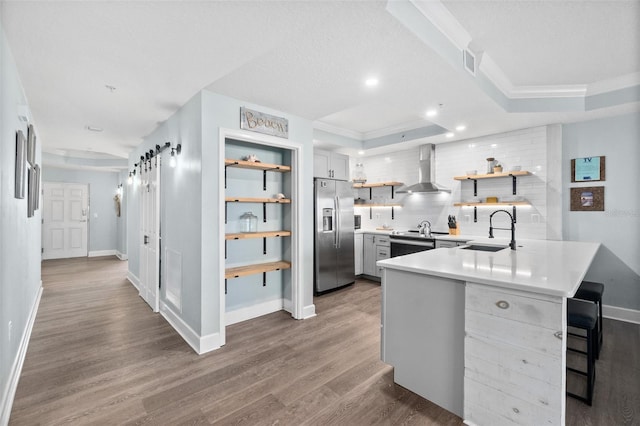 kitchen with appliances with stainless steel finishes, sink, kitchen peninsula, a raised ceiling, and wall chimney exhaust hood