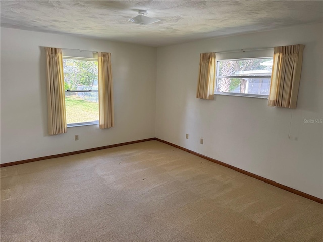 unfurnished room featuring plenty of natural light, baseboards, and light colored carpet