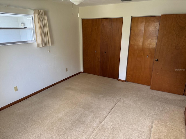 unfurnished bedroom featuring carpet floors, baseboards, and two closets