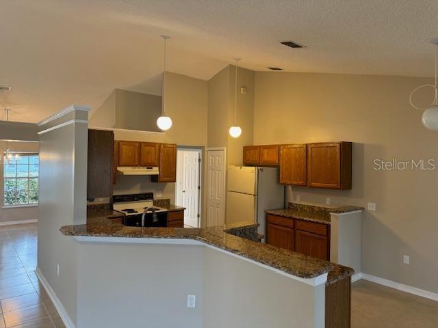 kitchen with decorative light fixtures, dark stone counters, white refrigerator, kitchen peninsula, and electric stove