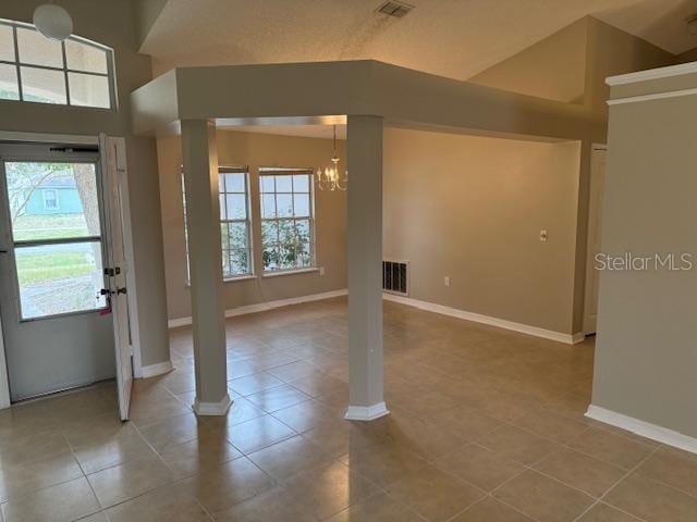 tiled entryway featuring lofted ceiling, decorative columns, a healthy amount of sunlight, and an inviting chandelier