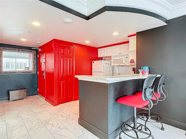 kitchen featuring sink, a breakfast bar area, white cabinets, kitchen peninsula, and white appliances