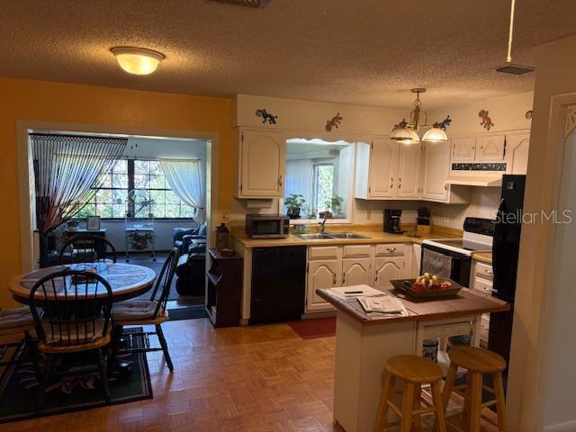 kitchen with pendant lighting, electric stove, a breakfast bar area, black dishwasher, and white cabinets