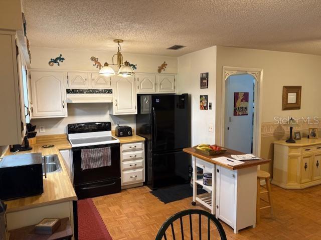 kitchen featuring black fridge, white cabinetry, decorative light fixtures, range with electric cooktop, and light parquet flooring