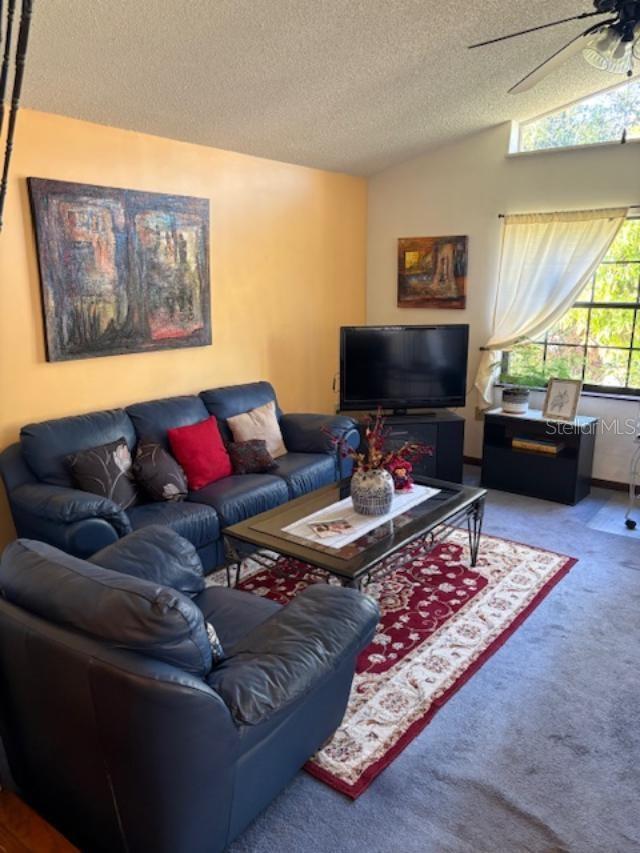 carpeted living room with vaulted ceiling, a textured ceiling, and ceiling fan