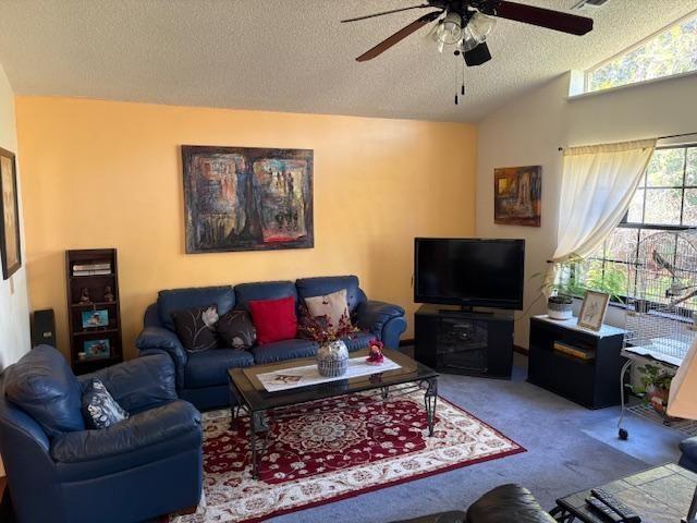 carpeted living room with ceiling fan, vaulted ceiling, and a textured ceiling