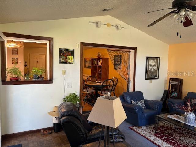 living room featuring vaulted ceiling, parquet flooring, ceiling fan, and a textured ceiling