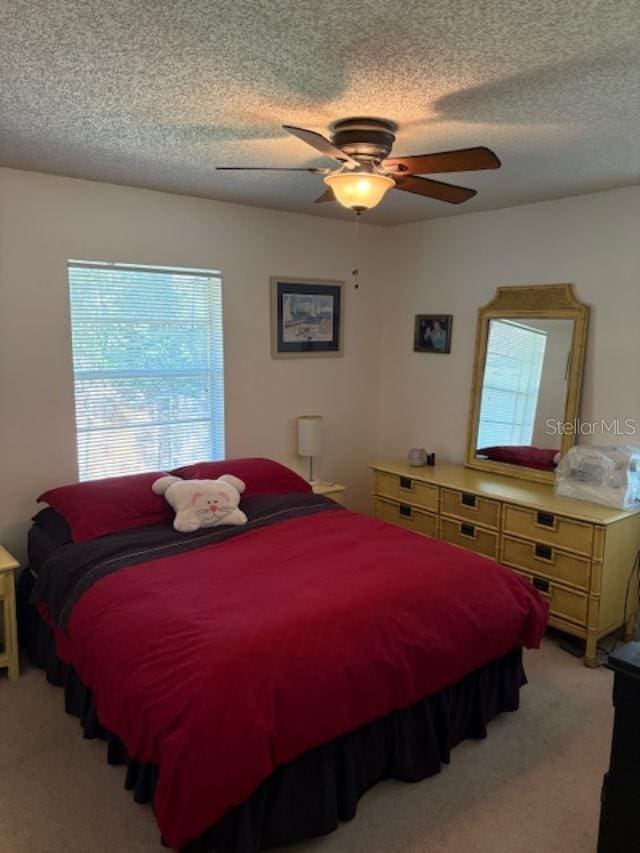 bedroom featuring ceiling fan, light colored carpet, and a textured ceiling