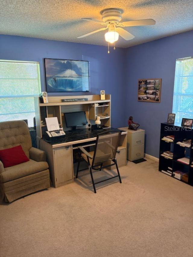 carpeted office space with a textured ceiling and ceiling fan