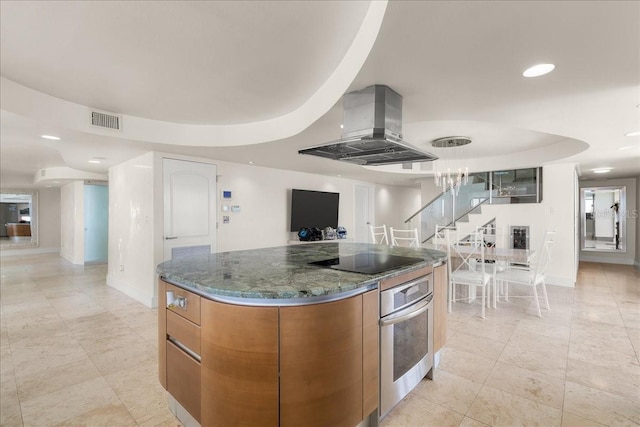 kitchen with stainless steel oven, black electric cooktop, a raised ceiling, island exhaust hood, and dark stone counters