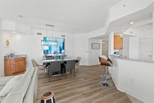 dining area with ornamental molding, sink, light hardwood / wood-style floors, and a textured ceiling