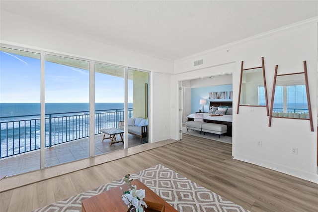 interior space featuring wood-type flooring, a water view, a textured ceiling, and crown molding