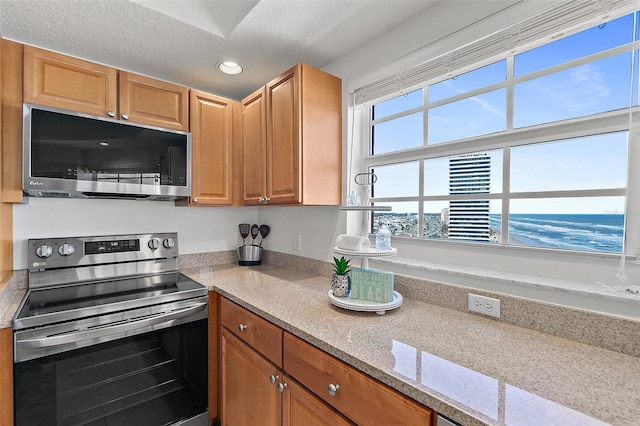 kitchen with light stone countertops, a water view, a textured ceiling, and appliances with stainless steel finishes