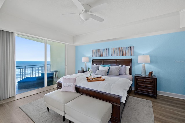 bedroom featuring a water view, hardwood / wood-style floors, access to exterior, and a textured ceiling