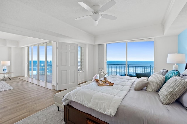 bedroom featuring multiple windows, a water view, access to outside, and light wood-type flooring