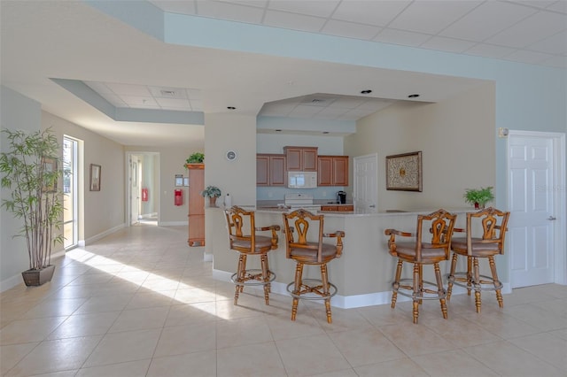 kitchen featuring a paneled ceiling, white appliances, a kitchen breakfast bar, and kitchen peninsula