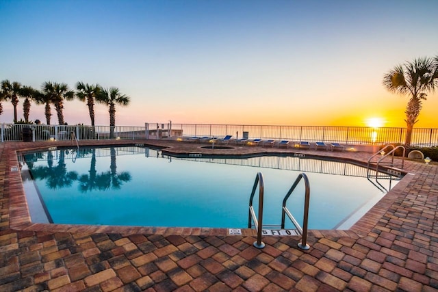 pool at dusk featuring a water view and a patio area