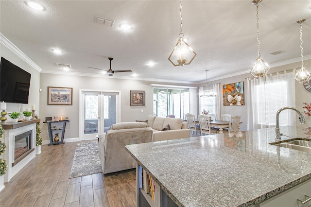 kitchen with hanging light fixtures, light stone countertops, hardwood / wood-style floors, sink, and a kitchen island with sink