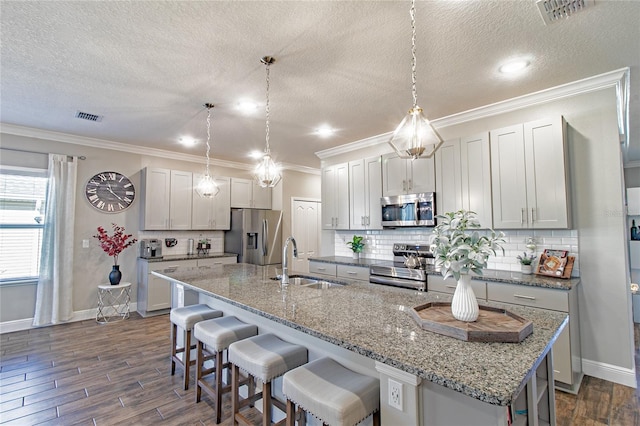 kitchen with sink, appliances with stainless steel finishes, a kitchen island with sink, and hanging light fixtures