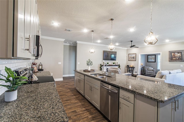 kitchen with an island with sink, sink, stainless steel appliances, and hanging light fixtures