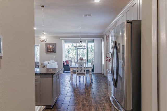 kitchen with dark hardwood / wood-style flooring, decorative light fixtures, stainless steel fridge, ornamental molding, and dark stone counters