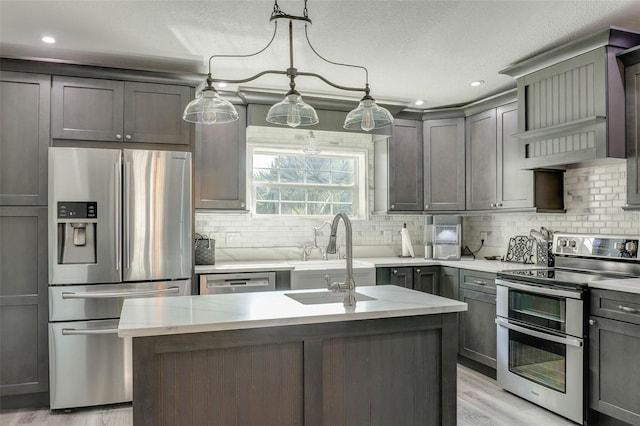 kitchen with a sink, wall chimney range hood, decorative backsplash, appliances with stainless steel finishes, and a kitchen island with sink