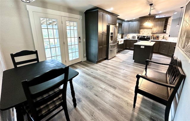 kitchen featuring light wood-type flooring, tasteful backsplash, a center island, appliances with stainless steel finishes, and light countertops