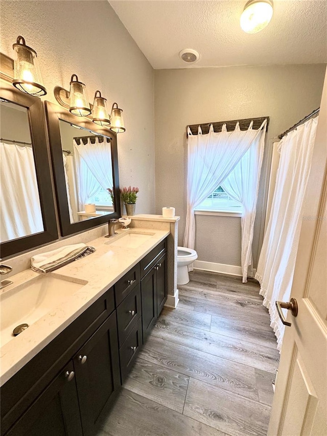 full bathroom featuring toilet, a textured ceiling, wood finished floors, and a sink