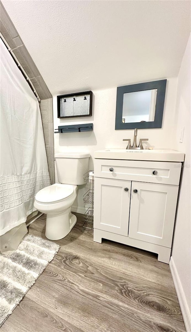 bathroom featuring baseboards, toilet, a shower with shower curtain, wood finished floors, and vanity