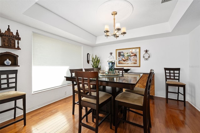 dining room with wood-type flooring, an inviting chandelier, and a tray ceiling