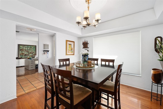 dining area featuring an inviting chandelier, hardwood / wood-style flooring, and a raised ceiling