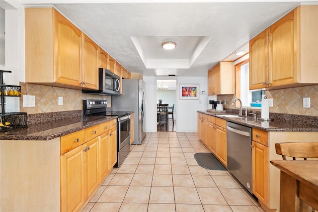 kitchen featuring sink, dark stone countertops, stainless steel appliances, a tray ceiling, and light tile patterned flooring