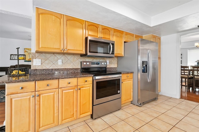 kitchen featuring light tile patterned floors, decorative backsplash, dark stone counters, and appliances with stainless steel finishes