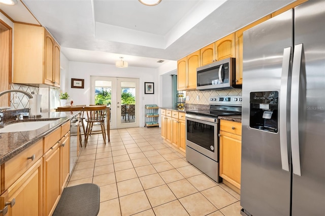 kitchen with a raised ceiling, sink, dark stone countertops, stainless steel appliances, and french doors