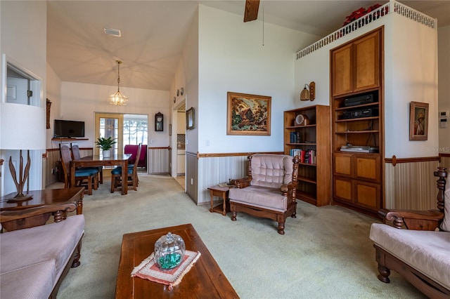 living area featuring high vaulted ceiling, light colored carpet, visible vents, wainscoting, and an inviting chandelier
