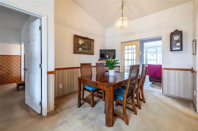 dining area with a wainscoted wall, vaulted ceiling, a chandelier, and light colored carpet