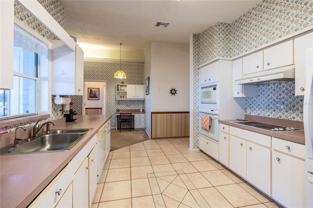 kitchen featuring under cabinet range hood, white appliances, a sink, visible vents, and wallpapered walls