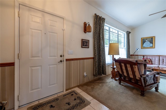 entrance foyer featuring light carpet, light tile patterned floors, wainscoting, lofted ceiling, and wood walls