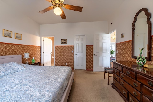 bedroom featuring light colored carpet, a wainscoted wall, ceiling fan, and wallpapered walls