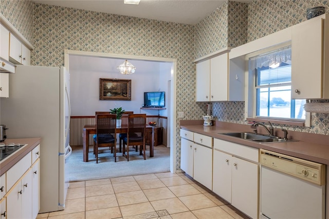 kitchen with white appliances, white cabinets, a sink, and wallpapered walls
